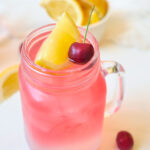 A single glass mug filled with Cherry Green Tea Lemonade and topped with a lemon wedge and a cherry.