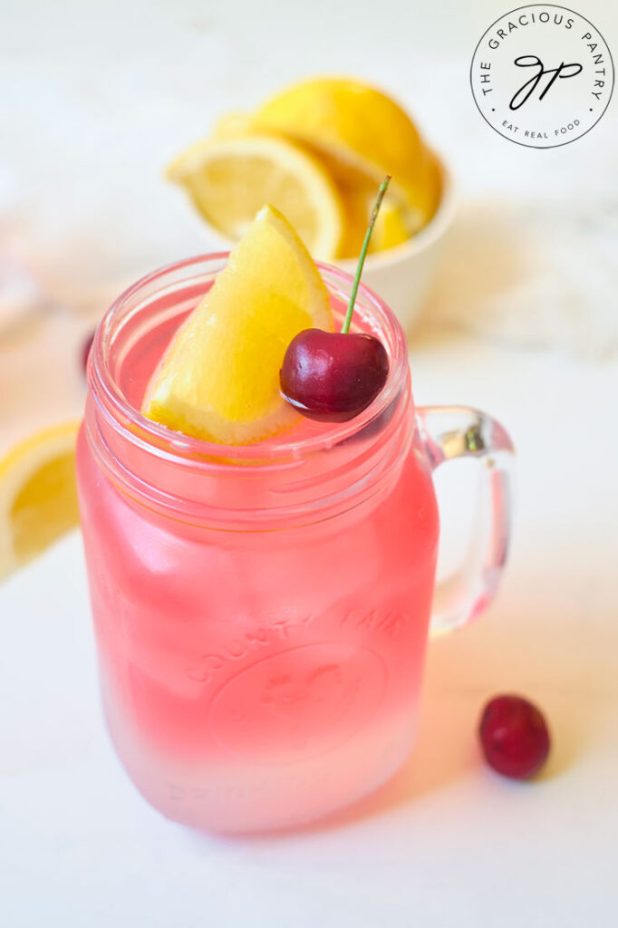 A single glass mug filled with Cherry Green Tea Lemonade and topped with a lemon wedge and a cherry.