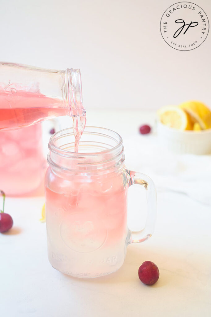 Pouring some brewed tea into a cup half way filled with lemonade.