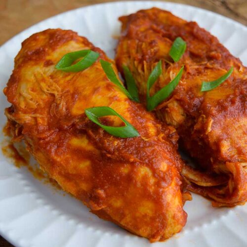 Two Crockpot BBQ Chicken Breasts sit on a white plate, topped with sliced green onions.