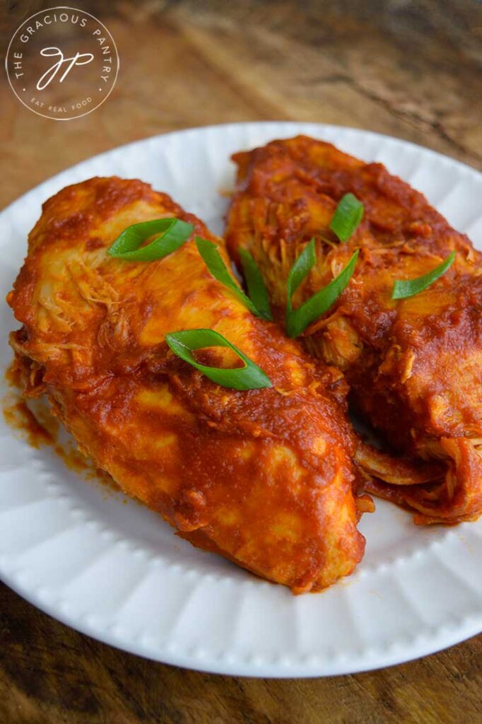 Two Crockpot BBQ Chicken Breasts sit on a white plate, topped with sliced green onions.