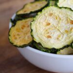 A side view of a white bowl filled with Dehydrated Zucchini Chips.
