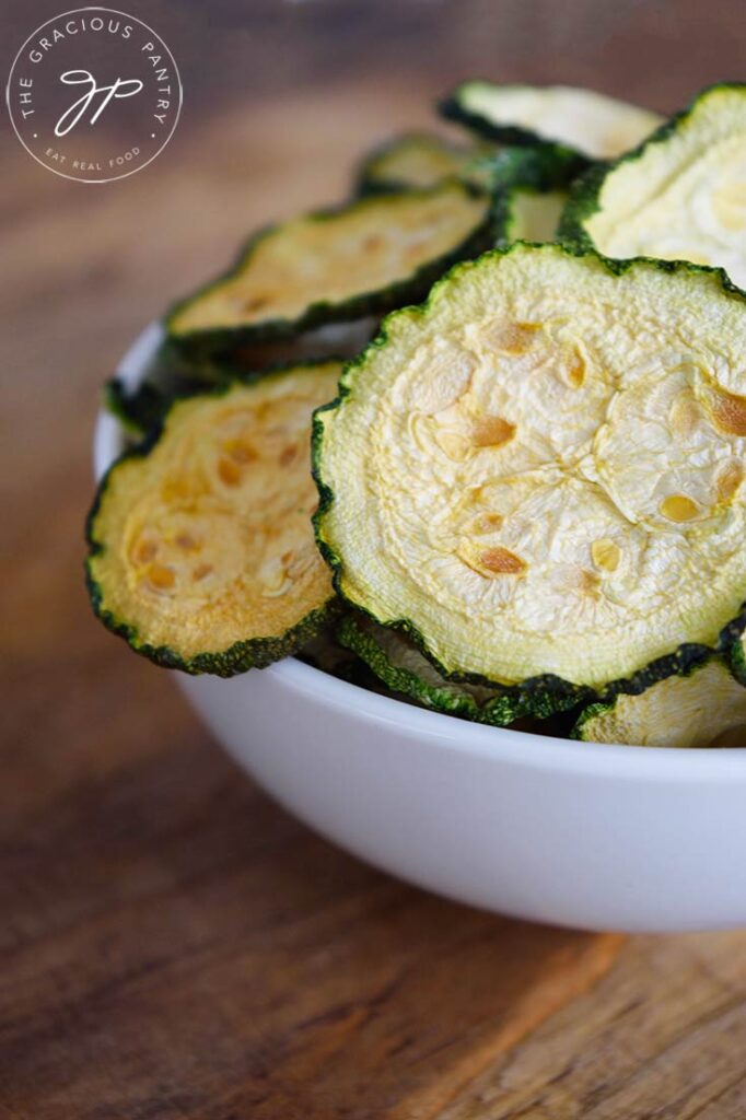 A side view of a white bowl filled with Dehydrated Zucchini Chips.