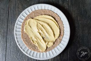A whole grain tortilla with hummus spread over it, on a white plate.