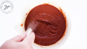 Whisking the Maple BBQ Sauce in a white mixing bowl.