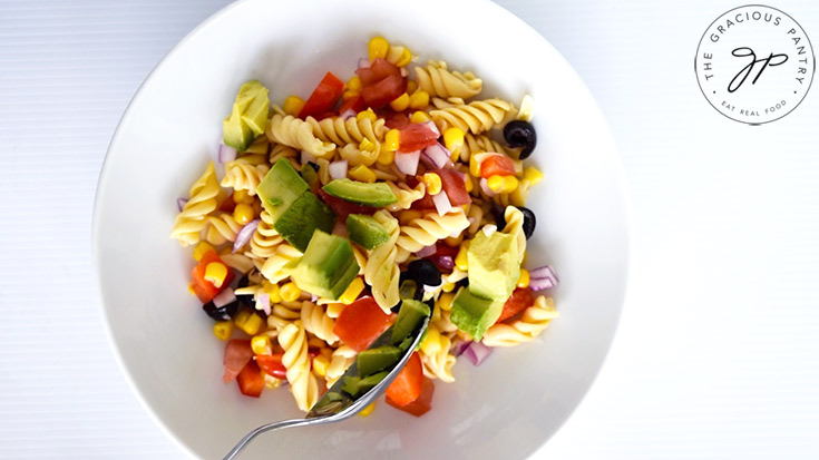 Serving chunks of avocado over the Mexican Pasta Salad in a white serving bowl.