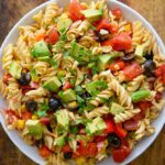An overhead shot looking down into a white bowl filled with this Mexican Pasta Salad. The bowl sits on a wooden surface.