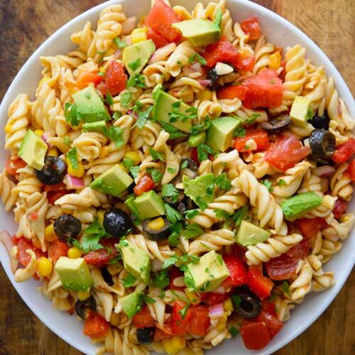 An overhead shot looking down into a white bowl filled with this Mexican Pasta Salad. The bowl sits on a wooden surface.