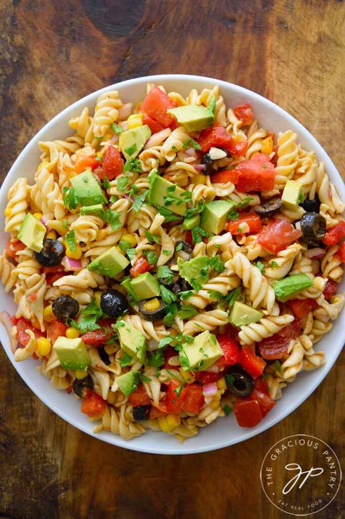 An overhead shot looking down into a white bowl filled with this Mexican Pasta Salad. The bowl sits on a wooden surface.