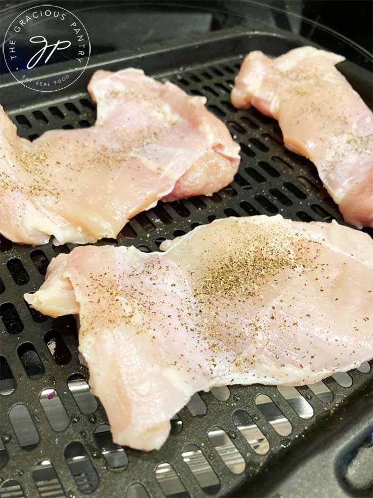 An air fryer tray with with three chicken thighs, sprinkled with salt and pepper.