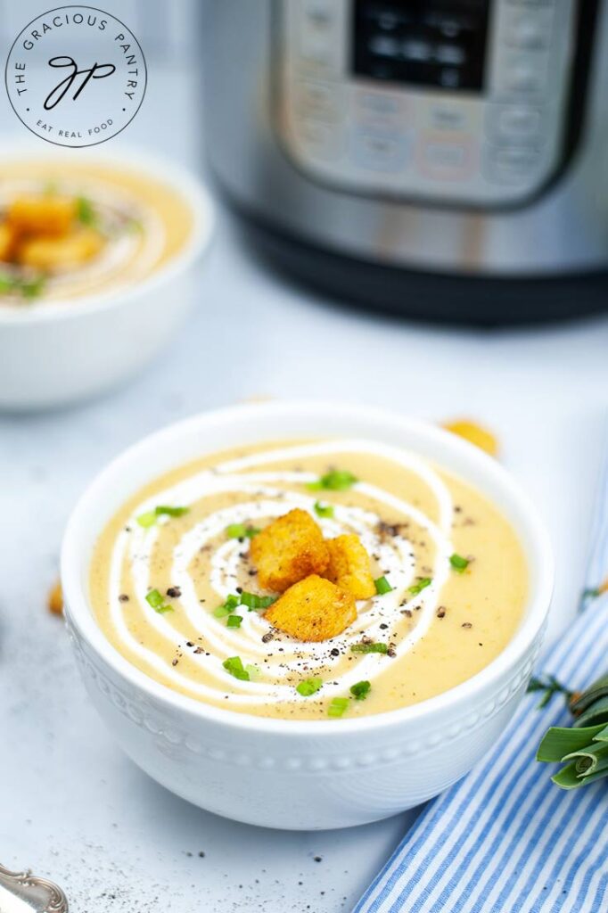 A side view of a single, white bowl filled with Instant Pot Potato Leek Soup and topped with croutons.