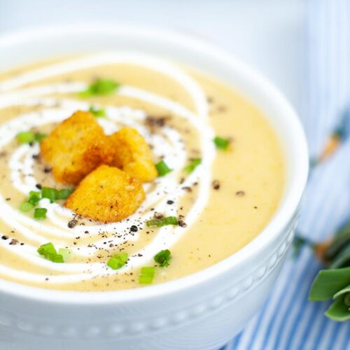 An up close shot of a bowl of Instant Pot Potato Leek Soup, topped with croutons and a swirl of cream.