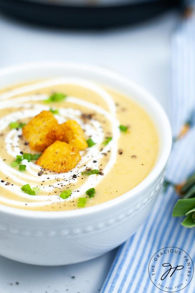 An up close shot of a bowl of Instant Pot Potato Leek Soup, topped with croutons and a swirl of cream.