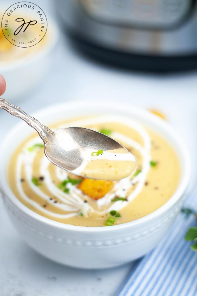 A spoon lifts a spoonful of Instant Pot Potato Leek Soup towards the camera.