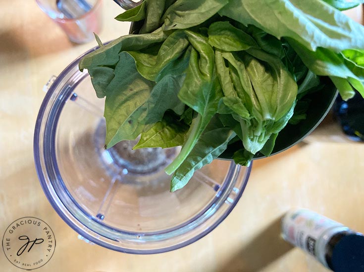 Fresh basil leaves being added to a blender cup.