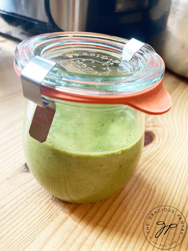 A small canning jar filled half way with this Lemon Basil Dressing Recipe. The lid is on and two metal clamps hold the lid down.