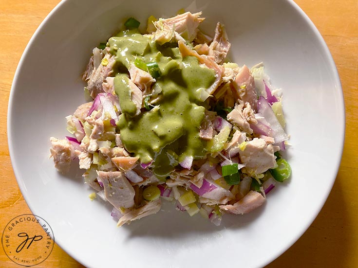 Lemon chicken salad served in a white bowl. Green, lemon basil dressing is drizzled over the top.