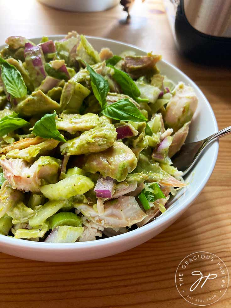 A side view of a white bowl filled with this lemon chicken salad. A fork rests on the side of the bowl.