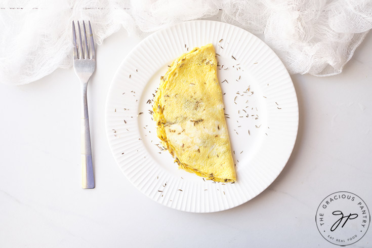 The finished One Egg Omelet on a white plate with a fork resting on the table to the left of the plate.