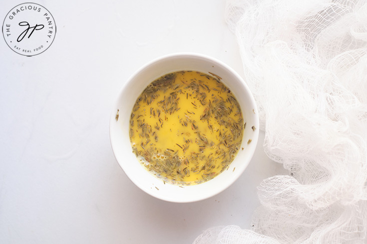 The egg mixture in a white bowl. You can see herbs floating on the top of the beaten eggs.