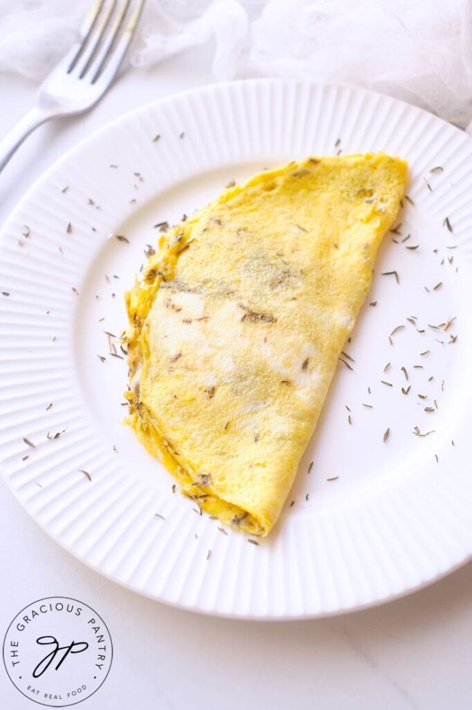 And up close shot of the One Egg Omelet on a white plate, sprinkled with dried herbs. A fork rests on the table to the top left of the shot.