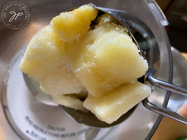 Adding frozen pineapple chunks to a food processor.