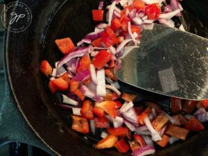 The peppers and onions being sautéd in a black, cast iron skillet.