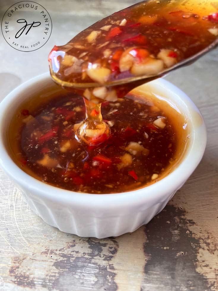 A close up of a spoon lifting some of the Thai Sweet Chili Sauce out of a white condiment bowl.