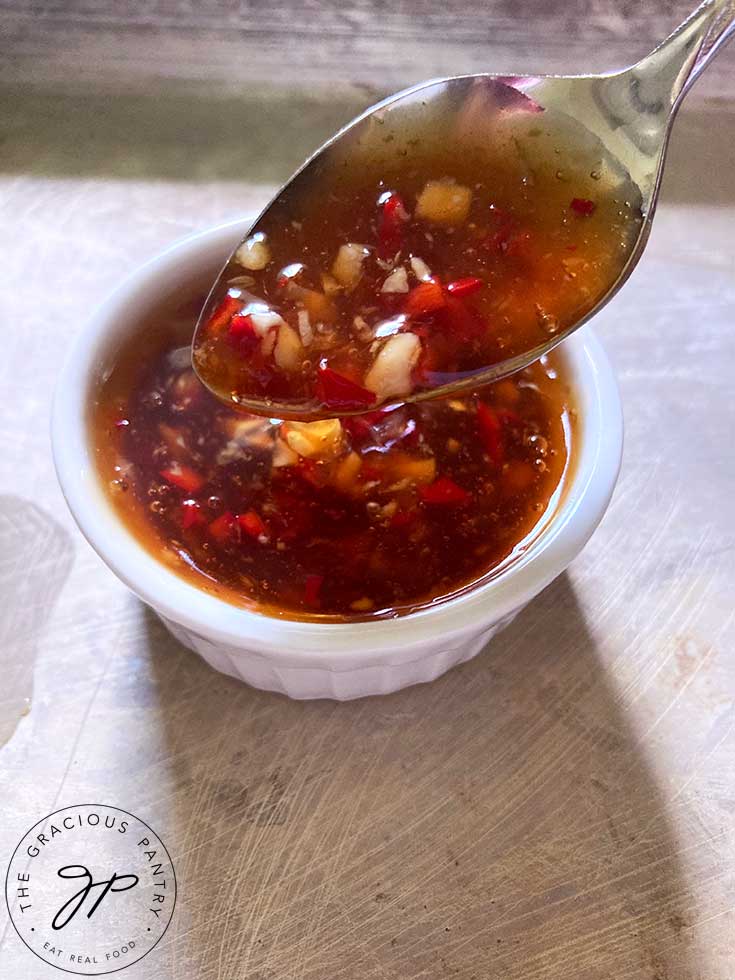 An overhead view of a spoon dipping into a small condiment bowl filled with this Thai Sweet Chili Sauce.