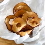 Air Fryer Apple Chips in crinkled parchment sitting on a wooden table.