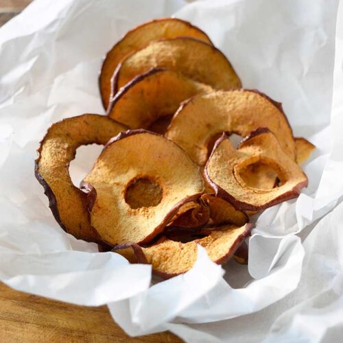 Air Fryer Apple Chips in crinkled parchment sitting on a wooden table.