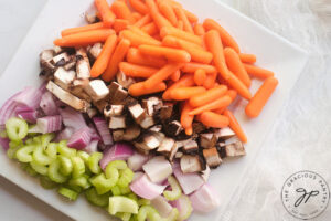 Cut celery, onions mushrooms and baby carrots on a white plate.