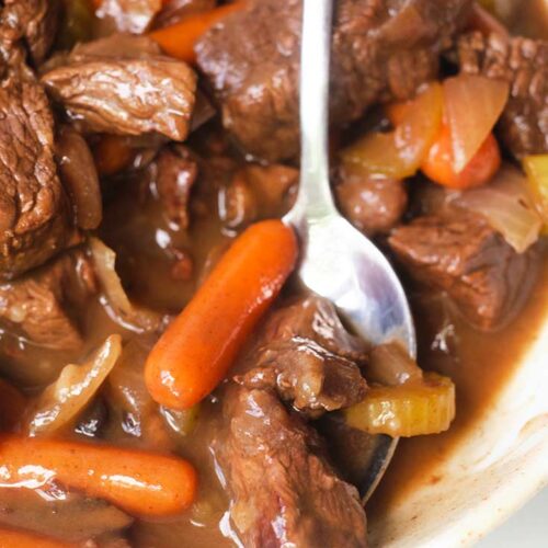 A white bowl with a silver spoon, picking up some of the bison stew from the bowl.