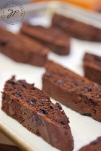 The sliced biscotti laying on a parchment-lined cookie sheet, ready for the second baking.