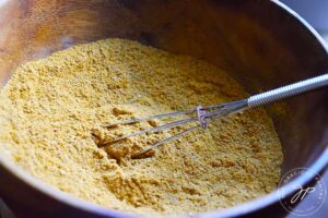 A side view of a wooden bowl filled with Jamaican Curry Powder.