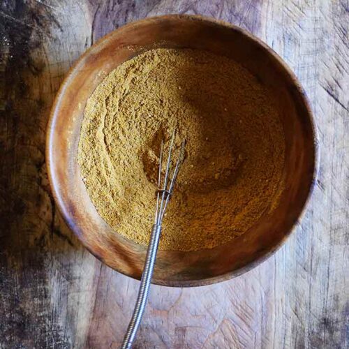 Dark mood lighting in this overhead shot of a wooden bowl filled with Jamaican Curry Powder.