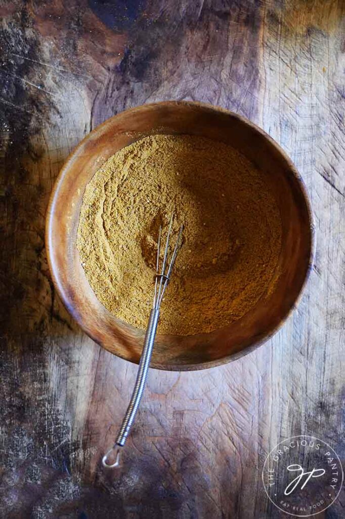 Dark mood lighting in this overhead shot of a wooden bowl filled with Jamaican Curry Powder.