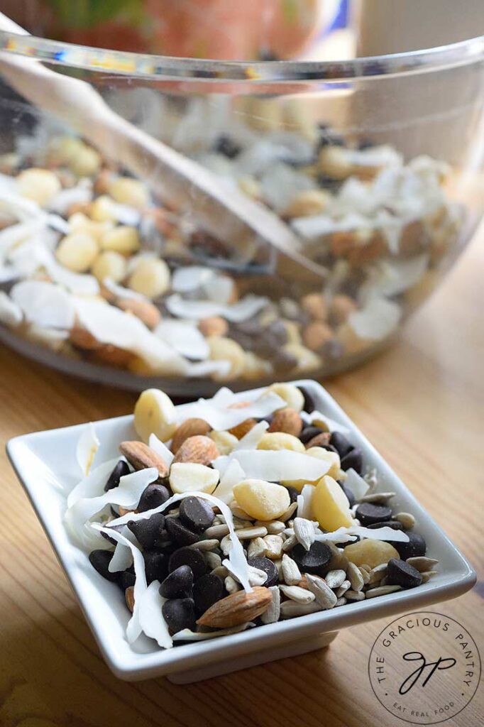 A small, white dish of Low Carb Trail Mix sits in front of a large, clean mixing bowl filled with more Low Carb Trail Mix.