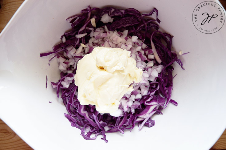 Mayo sitting on to of the onions in a white mixing bowl.