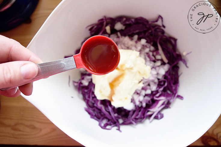 Holding a tablespoon measure of maple syrup over the mayo, ready to add it to this Red Cabbage Slaw Recipe.