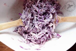 Tossing all the Red Cabbage Slaw Recipe ingredients together in a white mixing bowl.