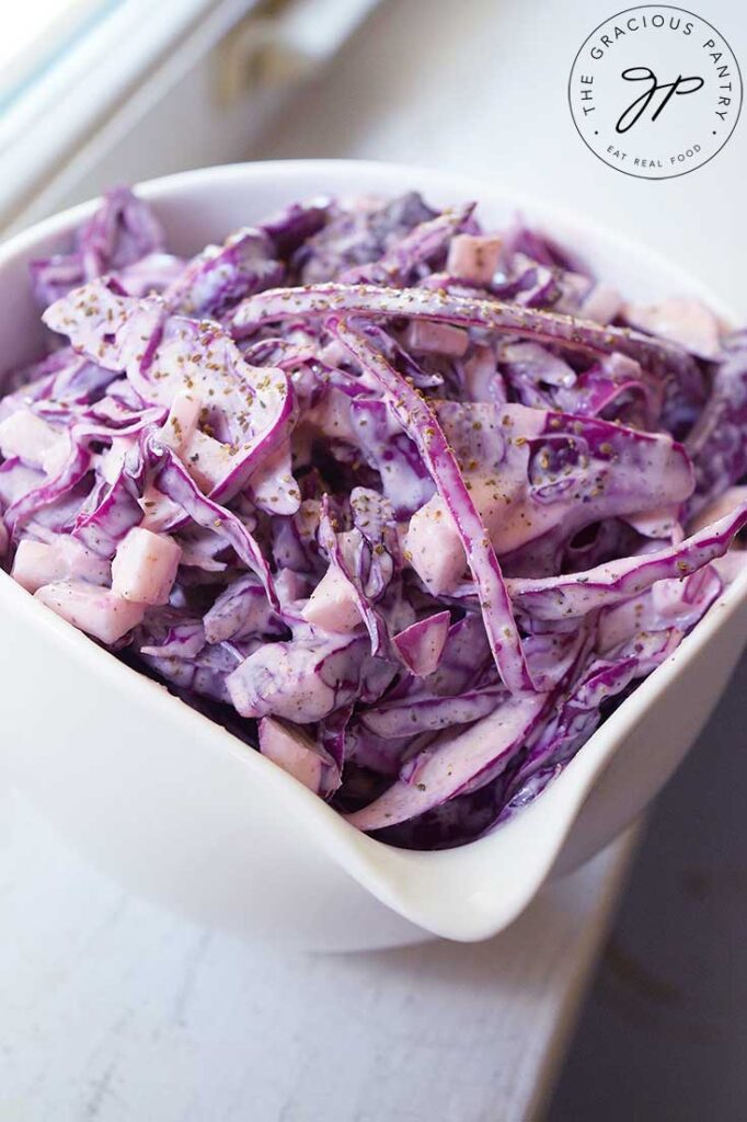 Another side view of a small white bowl sitting on a windowsill, filled with this Red Cabbage Slaw Recipe.