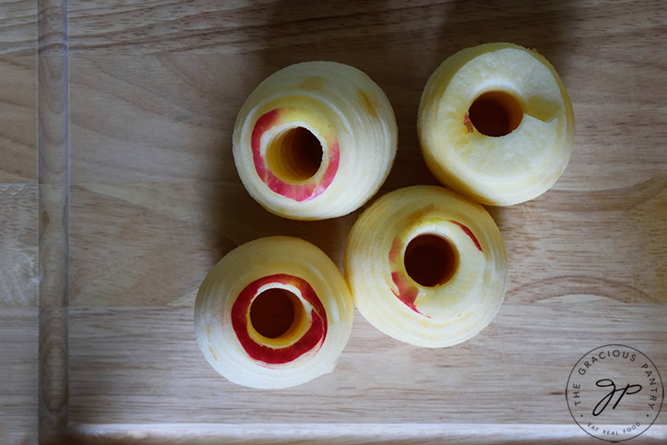 Four peeled and cored apples sitting on a cutting board.