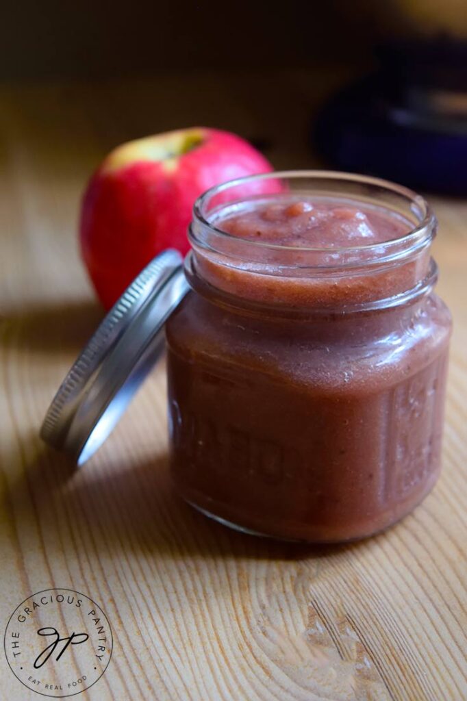 A canning jar sits filled with Strawberry Apple Sauce Recipe on a wooden table.