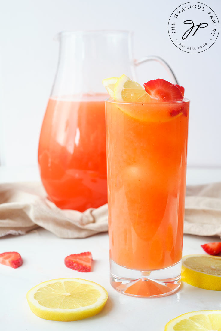 A tall, skinny glass, filled with Strawberry Lemonade and garnished with lemon and strawberry slices.