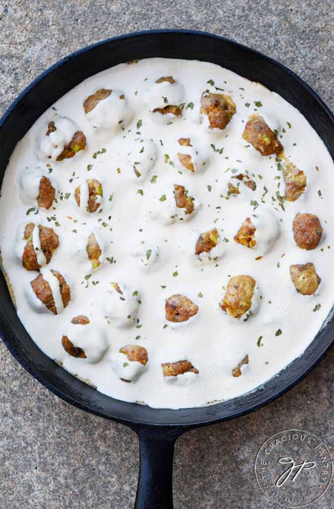 An overhead view looking down into a cast iron pan, filled with Swedish Meatballs sitting in a white sauce.