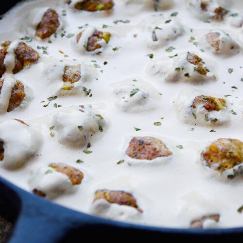 An up close view of Swedish meatballs sitting in a white sauce in a cast iron pan.