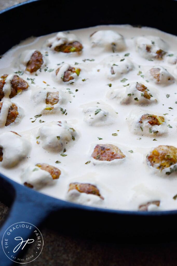 An up close view of Swedish meatballs sitting in a white sauce in a cast iron pan.