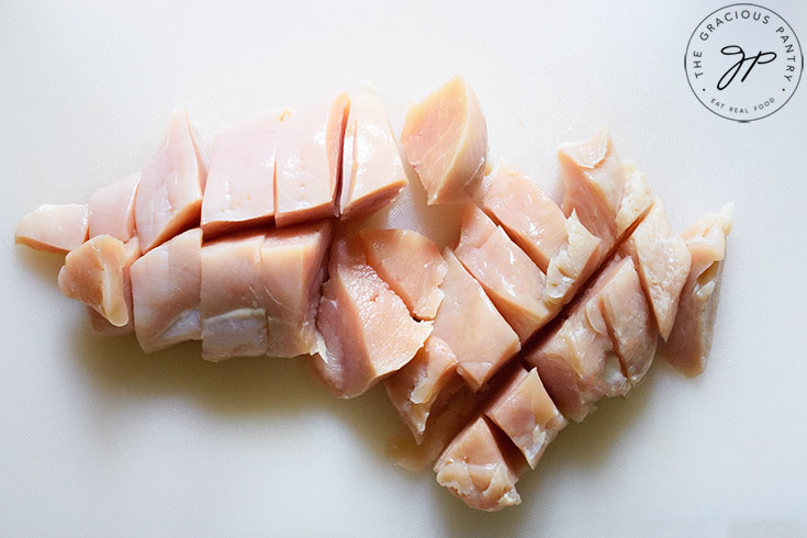 Two chicken breasts, cut into big chunks on a white cutting board.
