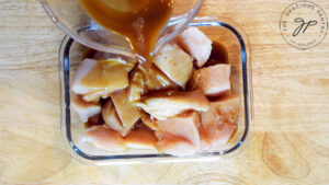 The cut chicken in a container getting teriyaki marinade poured over it.